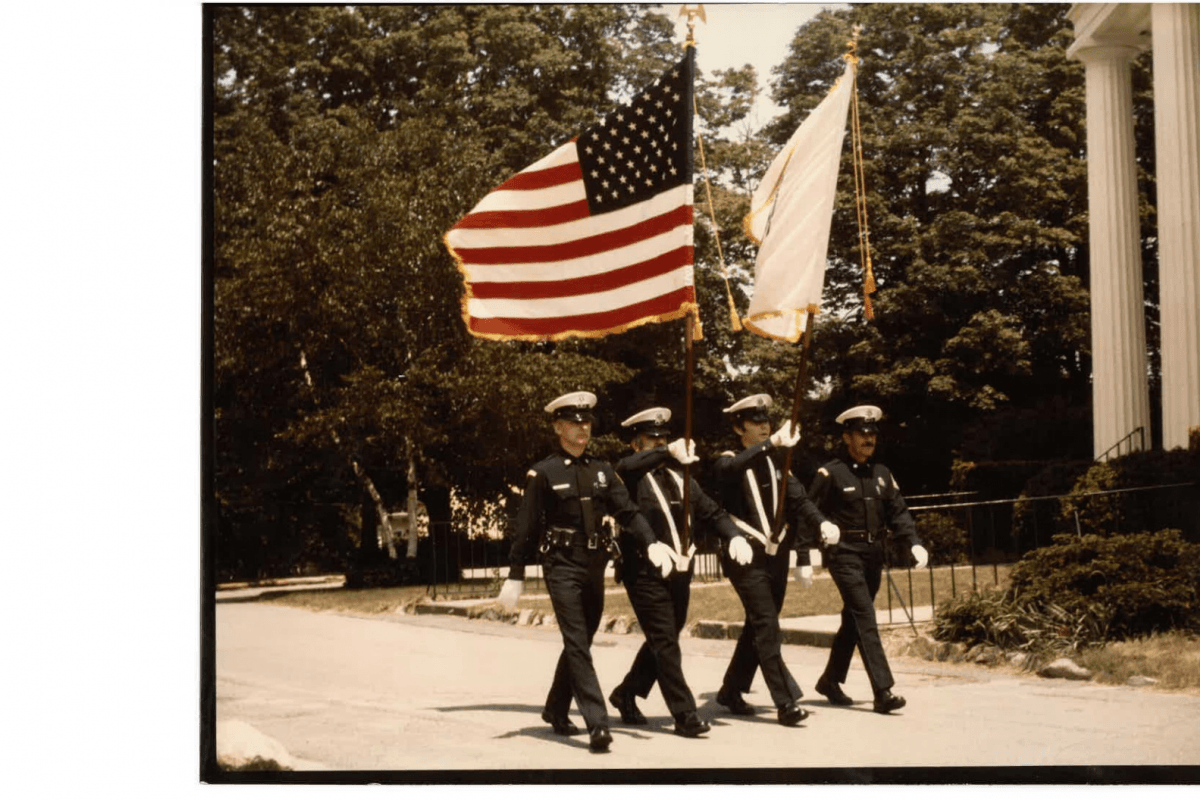 Four uniformed officers march while carrying flags
